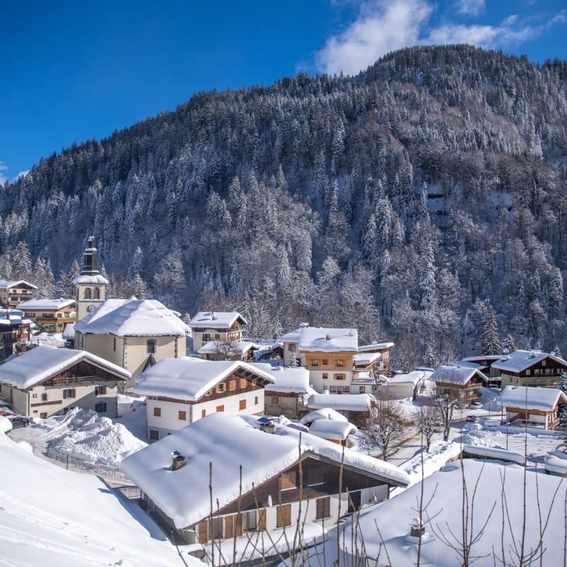 Vue en plongée du village de la Giettaz sous la neige et le ciel bleu.