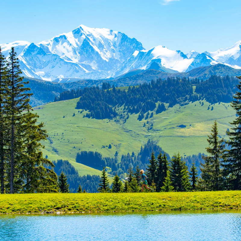 Trailer en train de courir à l'autre bout d'un lac ; en arrière-plan, le Mont-Blanc domine le paysage et les forêts de sapins.