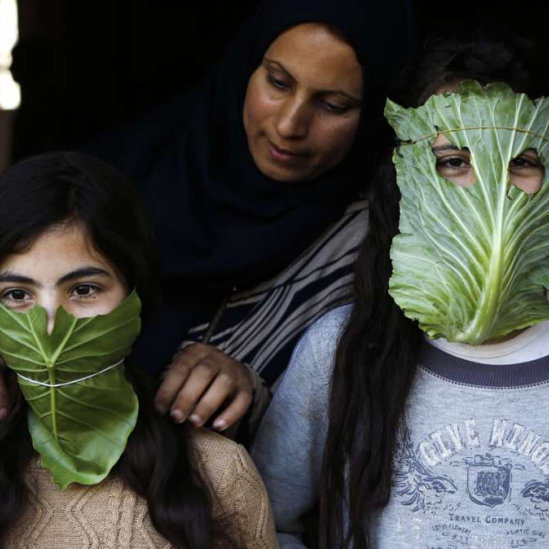 Le 16 avril 2020, une mère palestinienne distrait ses enfants avec des masques de fortune faits de choux dans le nord de la bande de Gaza lors de la pandémie COVID-19